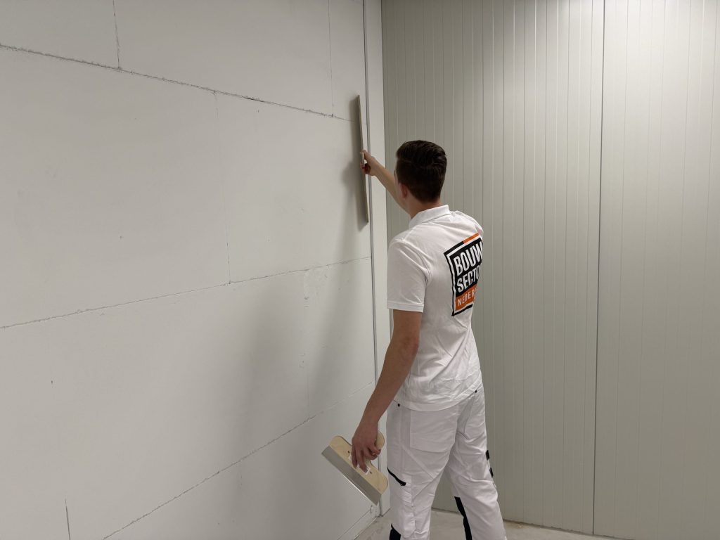 Stukadoor controleert met een lange spaan of een wand van gipsblokken vlak en recht staat