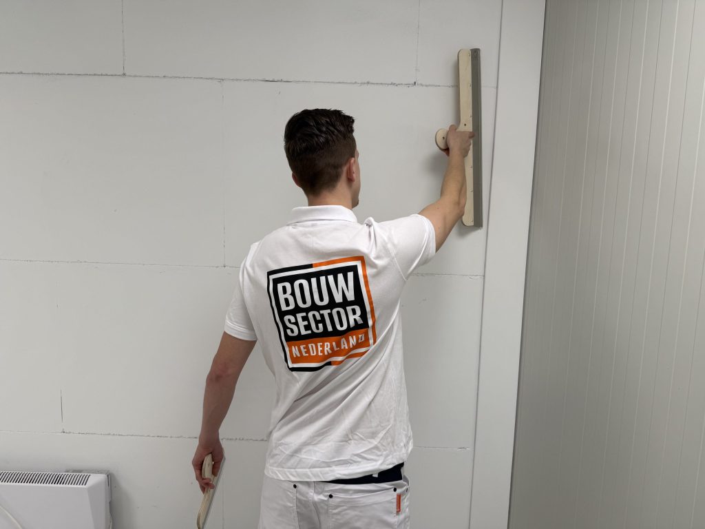 Stukadoor met pleisterspaan in de hand strijkt een witte wand glad met een lange spaan