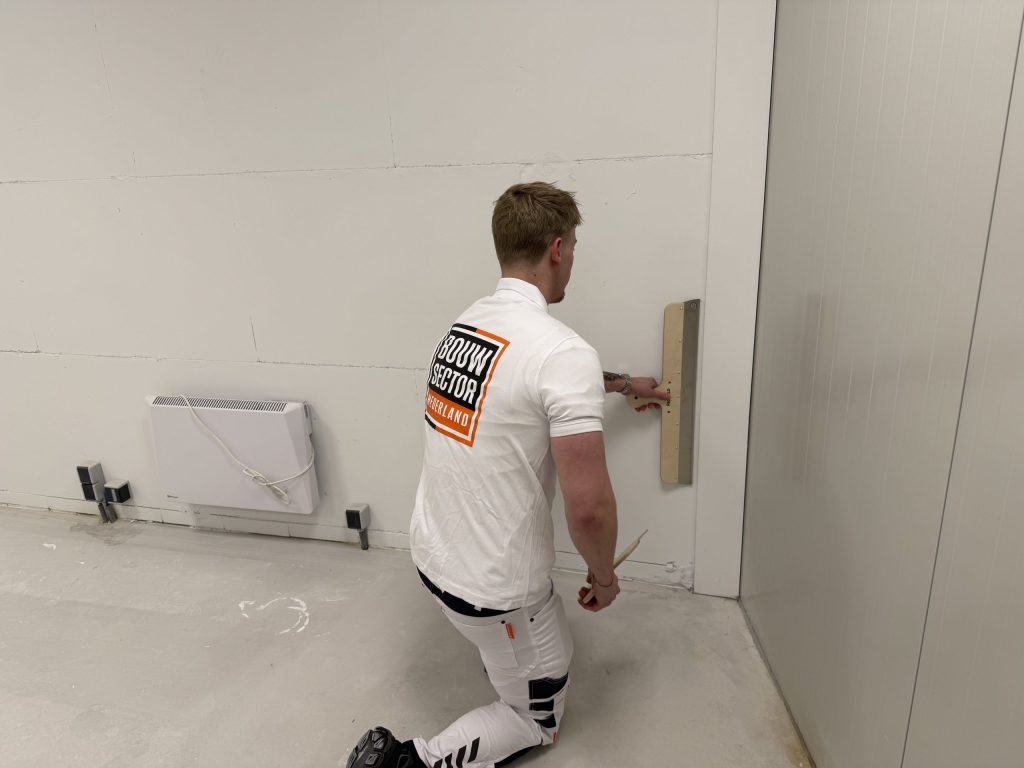Geknielde stukadoor werkt met een brede spaan het laagste stuk van een wand bij de hoek af